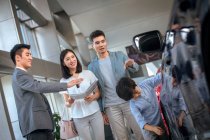 Asiatischer Verkäufer zeigt Auto für glückliche Familie im Autohaus — Stockfoto