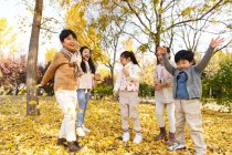 Cinq adorables enfants asiatiques jouer avec des feuilles jaunes dans le parc automnal — Photo de stock