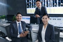 Professionelle Geschäftsleute lächeln in die Kamera, während sie gemeinsam im Kontrollraum arbeiten — Stockfoto