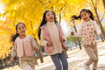 Three adorable happy asian kids running in autumnal park — Stock Photo