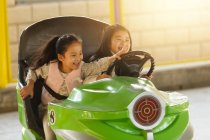 Adorable happy chinese girls riding car and playing together at playground — Stock Photo