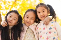Basso angolo vista di tre adorabile sorridente asiatico bambini abbracci in autunno parco e guardando fotocamera — Foto stock