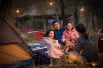 Mann spielt Gitarre für drei asiatische Freunde beim Zelten im herbstlichen Abendwald — Stockfoto