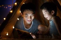 Happy asian father and preschooler son watching something on tablet in tent at home — Stock Photo