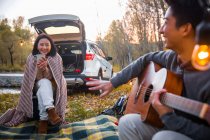 Happy asian boyfriend playing guitar for girlfriend in autumnal forest — Stock Photo