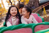 Felice ragazzo e ragazze seduti insieme sulle montagne russe nel parco — Foto stock