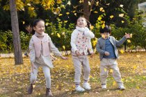 Niño feliz y niñas jugando juntos con hojas de otoño en el parque - foto de stock