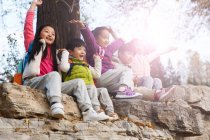 Cinco adorável feliz asiático crianças sentado no pedras com as mãos para cima no outonal parque — Fotografia de Stock
