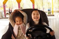 Чарівні щасливі китайські дівчата катаються на машині і грають разом на дитячому майданчику — стокове фото