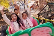 Happy chinese children sitting together on roller coaster in park — Stock Photo