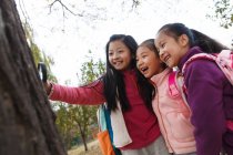 Three adorable asian kids hugging and looking at magnifying glass in autumnal park — Stock Photo