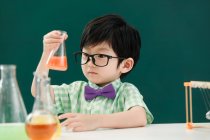 Adorable asiático escolar mirando bulbo en química clase en escuela - foto de stock