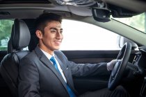 Vista laterale di bello sorridente asiatico uomo seduto in auto e guardando lontano — Foto stock