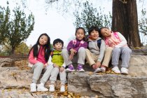 Cinco adorável asiático crianças sentado no pedras e olhando para câmera no outonal parque — Fotografia de Stock