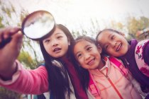 Drei entzückende asiatische Kinder, die sich im herbstlichen Park umarmen und auf die Lupe schauen — Stockfoto