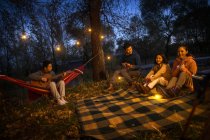 Uomo giocando chitarra per tre asiatico amici a campeggio in autunno sera foresta — Foto stock