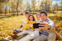 Four young smiling asian friends taking selfie with smartphone in autumnal forest — Stock Photo