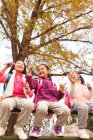 Low angle view of three adorable asian kids blowing soap bubbles in autumnal park — Stock Photo