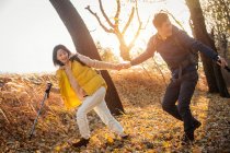 Smiling asian couple holding hands and trekking in autumnal forest — Stock Photo