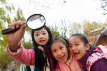 Три очаровательных азиатских ребенка обнимаются и смотрят на увеличительное стекло в осеннем парке — стоковое фото