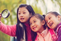 Trois adorables enfants asiatiques étreignant et regardant loupe dans le parc automnal — Photo de stock