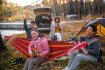 Asiatische Freunde spielen Gitarre und Ukulele beim Zelten im herbstlichen Wald — Stockfoto