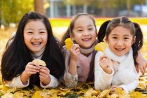 Три чарівні азіатські діти лежать на жовтому листі і тримають листя в автономному парку — стокове фото