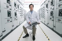 Technical personnel in lab coat working with laptop computer in the voltage room — Stock Photo