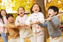 Пять очаровательных счастливых азиатских детей тянут верёвку вместе в осеннем парке — стоковое фото