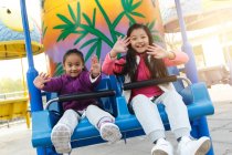 Filles heureuses jouant ensemble sur les montagnes russes dans le parc — Photo de stock