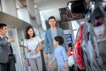 Asian seller showing car for happy family choosing vehicle at car showroom — Stock Photo