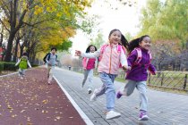 Five adorable asian kids running on road in autumnal park — Stock Photo