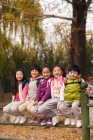 Cinq adorable sourire asiatique enfants assis sur la clôture et regardant caméra dans parc automnal — Photo de stock