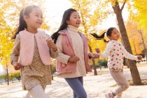 Three adorable happy asian kids running in autumnal park — Stock Photo