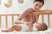 Bella giovane donna asiatica guardando adorabile neonato sdraiato in culla — Foto stock