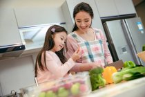 Happy young asian mother and adorable little daughter cooking together in kitchen — Stock Photo