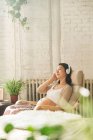 Jovem mulher grávida relaxada sentada na cadeira e ouvir música em fones de ouvido — Fotografia de Stock