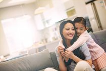 Feliz jovem asiático mãe com adorável pouco filha abraçando juntos no sofá — Fotografia de Stock