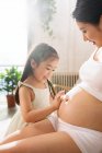 Чарівна маленька дитина торкається живота вагітної матері вдома — стокове фото