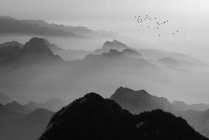 Black and white image of majestic dark mountains in fog, aerial view — Stock Photo