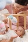 Glückliche junge Mutter blickt auf entzückendes Baby, das im Kinderbett liegt — Stockfoto