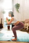 Visão lateral da jovem mulher grávida no treinamento sportswear em tapetes de ioga em casa — Fotografia de Stock