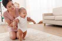 Felice giovane madre aiutare adorabile bambino in piedi su tappeto — Foto stock
