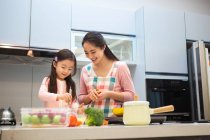 Sonriente joven madre en delantal con adorable pequeña hija cocinar juntos en la cocina - foto de stock