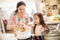 Beautiful happy young mother with adorable little daughter cooking together in kitchen — Stock Photo