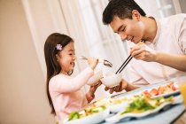 Happy азіатські батько і дочка тримають чаші з паличками для їжі і їдять разом вдома — Stock Photo