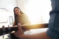 Cortado tiro de sorrindo jovem mulher olhando para namorado tocando guitarra em casa — Fotografia de Stock