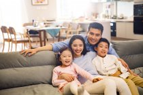 Щаслива азіатська сім'я з двома дітьми сидить разом на дивані і посміхається на камеру — стокове фото