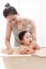 Happy young mother bathing adorable baby in bathtub with bubbles — Stock Photo
