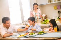 Щаслива Китайська сім'я з двома дітьми сидять за столом і їдять разом вдома — стокове фото
